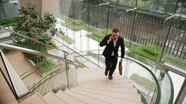 Akıllı iş adamı spiral merdivenlerden yukarı çıkıyor ve akıllı telefon kullanarak müdürü arıyor. Modern binada merdivenleri çıkarken telefonla pazarlama ekibinin üst düzey görüşü. Urbane.