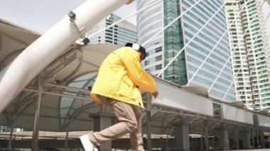 Asyalı şık bir adam alçak açılı kamerayla hip hop dansı yapıyor. Break dansçı, şehirde kulaklıktan müzik dinleyip dans ederken merdivenlerden çıkıyor. Açık hava sporu 2024. Yumuşak bir şekilde..