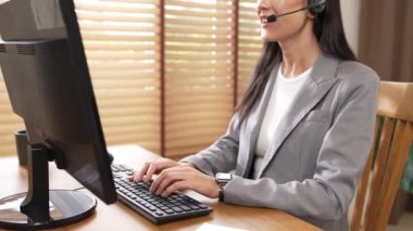 Kadın çağrı merkezi operatörü ya da müşteri hizmetleri çalışanı, müşteriye yardım etmek için kulaklıkla konuşurken çalışma alanı üzerinde çalışıyor. Profesyonel modern iş hizmeti. Blithe