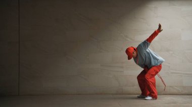 Yakışıklı koreograf gri arka planda sokak dansı yapıyor. Genç çekici erkek dansçı şık kıyafetler giyerken gösteri yapıyor. Hareketli bir adım. Uzayı kopyala Açık hava sporu 2024. Yumuşak bir şekilde..