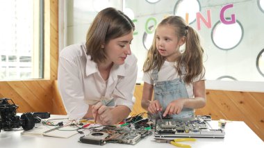 Genç, zeki, beyaz bir öğretmen öğrencilere elektronik kurulun bir parçasını öğretiyor. Uzman kız dijital elektrikli aletleri öğreniyor ve cips ve kablolarla ana kartı tamir ediyor. Etkinlik.