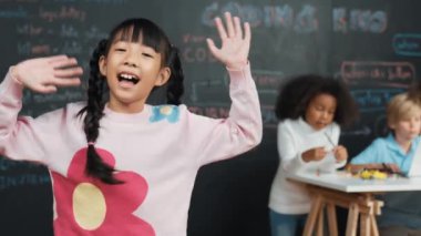 Asyalı kız gülümseyip kameraya el sallarken arkadaşı çalışıyor ya da mühendislik şifresi öğreniyor ya da BTMM teknoloji sınıfında acele ediyor. Çocuklar dizüstü bilgisayar kullanırken çocuk kameraya bakıp selam veriyor. Etkinlik.