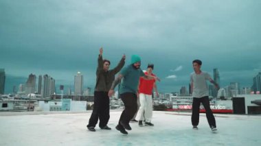 Profesyonel hippi hareketsiz poz verirken aynı zamanda şehir manzaralı çatıdaki müziğe ayak basıyor. Break dansçı, hip-hop dansçıları grubuyla birlikte sokak dansı yapıyor. Açık hava sporu 2024 hiphop..