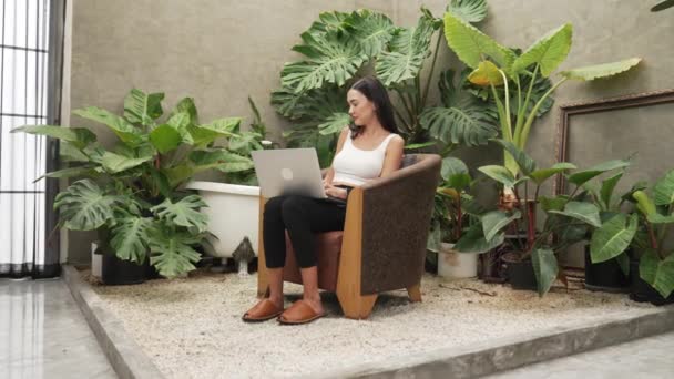 現代の若い女性は 携帯電話で話したり リモートで作業したり 最小限の建築コンクリートスタイルの夏のエキゾチックな植物の葉庭の孤独の中でリラックスしたりします ブリテット — ストック動画