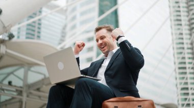 Profesyonel iş adamının merdivenlerde dizüstü bilgisayarla çalışırken başarılı bir projeyi kutlamasının düşük açılı görüntüsü. Kafkas proje yöneticisi şehir merkezinde pazarlama stratejisi planlamak için bilgisayar kullanıyor. Urbane.