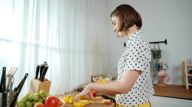 Kafkaseli anne kahvaltıda sebze pişirirken mutlu anne de modern mutfakta salata için taze malzemeler hazırlıyor. Hizmetçi sağlıklı yemek pişiriyor. Dikkat konsepti. Pedagoji.