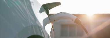 Otoparkta EV elektrikli araba şarj bataryası var. Şehir merkezinde gün doğumu ışığı var. Sürdürülebilir ve çevre dostu seyahatler için yeniden şarj edilebilir araba için alternatif enerji teknolojisi.