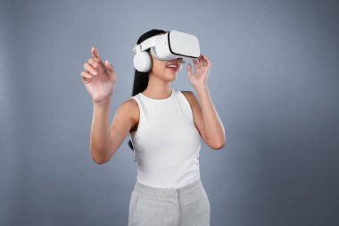 Gri arka planı olan zeki bir kadın metaevrene bağlı VR kulaklık takıyor, gelecekçi siber uzay topluluğu teknolojisi. Zarif bir kadın sanal bir manzara gördüğü için heyecanlı. Halüsinasyon.