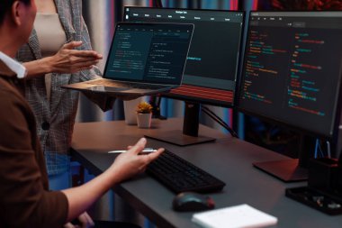 Modern ofisteki neon ışık odasında bilgi ağını gösteren dizüstü bilgisayarla iki ekranda veri çalıştıran akıllı web sitesi geliştirme kodlayıcı sistemini tartışan IT geliştiricilerinin ciddiyeti. İnfobahn.