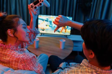 Joystickli birkaç oyuncu dövüş oyunu oynuyor, kadın oyuncu yarışması derecesi arka tarafta TV ekranında modern rahat evinde neon ışıklı oturma odasındaki koltukta oturuyor. İnfobahn.