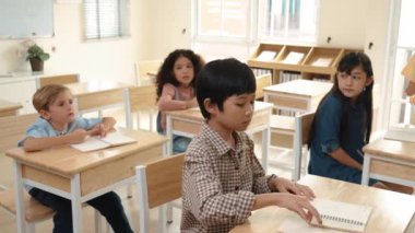 Sınıf çalışması yapan Asyalı yetenekli bir öğrenci ya da sınıfta otururken test yapıyor. Çeşitli çocuklar kağıda yazıyor ya da sınıfa katılırken not alıyorlar. İlkokul konsepti. Pedagoji.