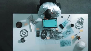 Türbin motoru veya jet motoru tasarımı ve çeşitli metal teçhizat dağılımı ile toplantı masasında yeşil ekranlı tablet üzerinde çalışırken telefona bakan mühendis görüntüsü. Hizalama.