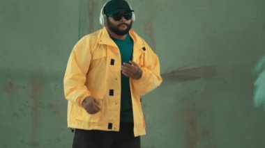Profesyonel hipster sokak, şehir merkezinde ayak sesleri gösteriyor ya da pratik yapıyor. Genç break dansçı hareket ediyor ve kolunu ve bacağını esnetiyor. Açık hava sporu 2024. Gri arka plan. Hip hop modası. hiphop.