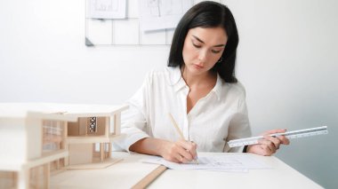 Closeup portrait image of professional young beautiful engineer architect using triangular scale measures house model with focusing at modern office. Business creative design concept. Immaculate. clipart