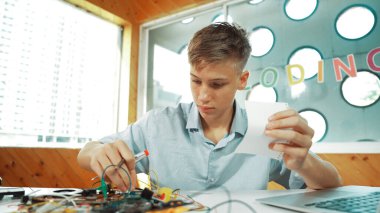 Akıllı çocuk notlara bakarken elektronik alet kullanmayı öğrenir ya da inceler. Lise öğrencisi STEM teknoloji sınıfında otururken elektrikli aletler üzerinde çalışıyor ya da teftiş yapıyor. Öğretim.