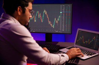 Akıllı tüccar işadamı, karanlık oda gecesinde neon ışıklı ofisteki arama pazarında yüksek kârla ekranda bilgisayar ve bilgisayar üzerinde dinamik borsa yatırımları üzerinde yoğunlaşıyor. Tahmin et..