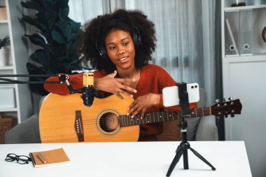 Genç Afrikalı Amerikalı müzisyenin sunucu kanalı gitar çalıyor, şarkı söylüyor, stüdyoda akıllı telefondan yayın yapıyor. Ekipman kulaklıkları dekorasyonu ve mikrofon kaydı. Tatlandırıcı.