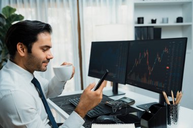 Elinde telefon dinamiğine odaklanan kahve fincanı tutan borsa yatırım ekranı veri analizini karşılaştırarak iç işlerinde yüksek kârlı finans teknolojisi pazarına yatırım yapıyor. Tahmin et..