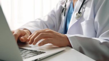 Hastanedeki doktor masasında oturup dizüstü bilgisayar üzerinde çalışıyor. Hasta test sonuçlarını teşhis ediyor, hastalıklar ve hastalıklar için tedavi planı geliştiriyor. Sağlık personeli ve sağlık hizmetleri. Ağır çekim. Katı.