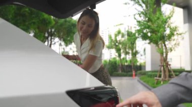 Yaz mevsiminde yeşil sürdürülebilir şehir bahçesinde ağır çekimde çalışan EV elektrikli araba yeşil sürdürülebilir şehirde yeniden şarj edilebilir elektrikli araç iç organları için alışveriş yapan genç çiftlerin yaşam tarzını gösteriyor.