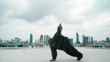 Profesyonel B-boy dansçısı, profesyonel sokak dansçısı. Çatıda gökyüzü dövüşçüsü, şehir manzaralı. Çekici Asyalı hipster enerjik adımlar atıyor. Break dans. Açık hava sporu 2024 hiphop..