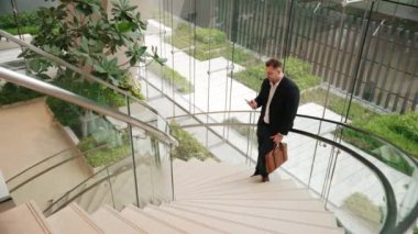 Mutlu iş adamı başarılı projesini ve menajerini akıllı telefon kullanarak kutluyor. Erkek lider, modern binada merdivenlerde dururken telefonla pazarlama ekibini konuşuyor. Urbane.