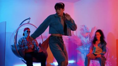 Çok kültürlü bir arkadaş kürsüde otururken Asyalı yetenekli bir dansçı modern müziğe geçiyor. Profesyonel dansçı, hipster takımı tezahürat yaparken ve desteklerken enerjik adımlar atıyor. Mutluluk.