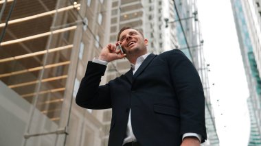 Düşük açılı kamera görüntüsü, iş adamının yöneticiyi ararken gökdelen manzaralı iş planını tartışır. Profesyonel proje yöneticisi telefonla çalışıyor ve pazarlama fikirlerini paylaşıyor. Urbane.