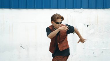 Beyaz arka planda break dans pratiği yapan yakışıklı bir sokak dansçısı. Hip hop tarzı giyinen sporcu, mavi arka planlı bir sokakta müzik eşliğinde ayak sesleri çıkarıyor. Açık hava sporu 2024. ÇalışmaComment.