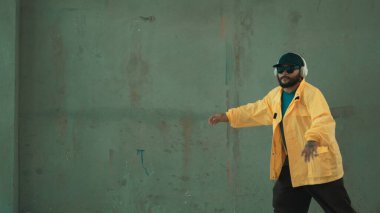 Hippi sokak, şehir merkezinde ayak izleri gösteriyor ya da pratik yapıyor. Hareketli genç break dansçı hareketi ve kol ve bacak esneme hareketi. Açık hava sporu 2024. Gri arka plan. Hip hop modası. ÇalışmaComment.