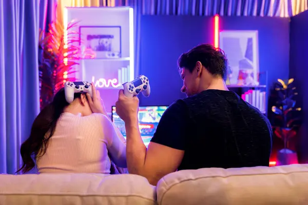 バックサイドビューで女性敗者挑戦横のビデオゲームで戦う男の勝者 赤い青いネオンライトの電球のスタジオルームでジョイスティックを使用してテレビで遊ぶカップル楽しい ポストレート — ストック写真