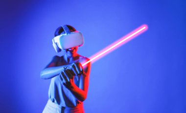 VR kulaklık takan zeki bir kadın metaevrene bağlanıyor, gelecekteki siber uzay topluluğu teknolojisi. Kılıç dövüşü oynarken lazer kılıcını sıkıca tutan zarif bir kadın. Halüsinasyon.