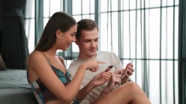 Genç çift, kredi kartıyla ödemek için internet üzerinden ödeme uygulaması ve dijital cüzdan kullanarak yatak odasında oturuyor. Mobil internet üzerinden alışveriş ve modern alımlar. Düzenle