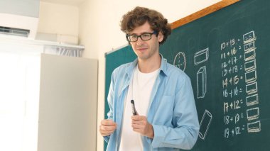 Caucasian teacher looking at student while standing at blackboard. Low angle camera of professional instructor teaching and explain math theory while answer question from diverse student. Pedagogy. clipart