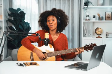Genç Afrikalı Amerikalı müzisyenin sunucu kanalı gitar çalıyor, şarkı söylüyor, stüdyoda dizüstü bilgisayardan yayın yapıyor. Kulaklık dekorasyonu ve mikrofon kaydı. Tatlandırıcı.
