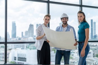 Bir grup zeki mimar proje planlarını tutarken kameraya bakıyor. Kaliteli yönetici takımı inşaat hakkında konuşurken şehir manzaralı bir yerde duruyor. Ekip çalışıyor. İzleme.