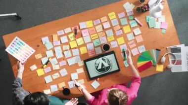 Tablet ekran logosu tasarımı ile toplantı masasında otururken renkli yapışkan notlar üzerine tasarımcı yazma fikrinin üst görünümü. Tasarım yapan ve karar veren profesyonel bir iş kadını. Sempozyum.