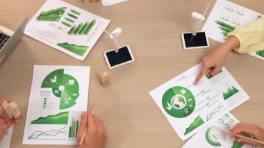 Eko evi projesini yel değirmeni tasarım modeli ve karbon ayak izini azaltmak için yeşil enerji kullanım grafiği ile toplantı masasında tartışan harika bir iş ekibi. Dünyayı kurtarın. Eline odaklan. Tanımlama.