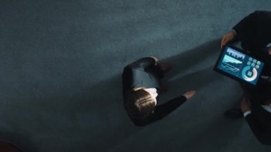 Zeki yöneticinin çeşitli takımlarla tokalaştığı ve tabletteki finansal verileri analiz ettiği yukarıdan aşağıya hava görüntüsü. Kadın lider bir anlaşma yaparak gruba katılıyor ve pazarlama stratejisini paylaşıyor. Müdürlük.