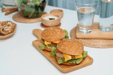 Kare saplı ahşap tahtada çift dev kızarmış hamburger yemeğine odaklanıyorum. Salatayla süslenmiş, ev yapımı çörek, beyaz masadaki fast food konseptinde su içmenin yanı sıra. İnfobahn.
