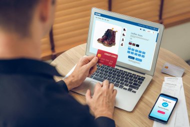 Genç adam internet bankacılığı için kredi kartlı dizüstü bilgisayar kullanıyor. İnternet üzerinden alışveriş yapıyor. Banka kartıyla modern ve kullanışlı online satın alma. Açılıyor