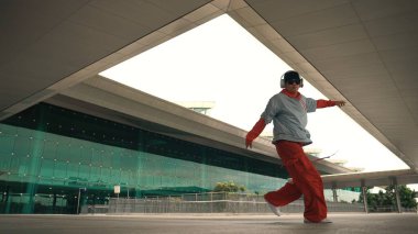 Serbest dans ederken müzik dinleyen profesyonel hipsterin hareketli çekimi. Sokak dansçısı hareket ediyor, el sallıyor ve break dansın tadını çıkarıyor. Modern yaşam tarzı. Açık hava sporu 2024. Yumuşak bir şekilde..