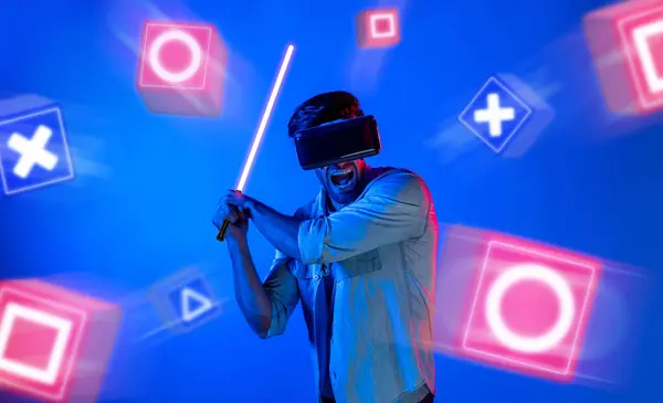 音楽ブロックでネオン剣をフェンシングするVrメガネを持つエネルギッシュな男 剣を持ってゲームをするプロのゲーマーは青い背景とメタバースに入ります バックグラウンド デバイス — ストック写真