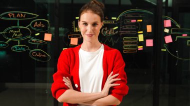 Profesyonel genç yönetici, silah zoruyla kameraya bakıyor. Cam duvarın önünde zihin haritası ve yapışkan notlarla dikilen yetenekli bir işçi. İzleme