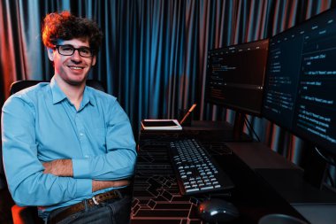 Ekranda yazılım geliştirme bilgisine karşı oturan gülümseyen bilişim geliştiricisinin profili, web sitesindeki son sürüm uygulaması için program kodlaması oluşturarak çevrili kameraya bakıyor. Toplayıcı.