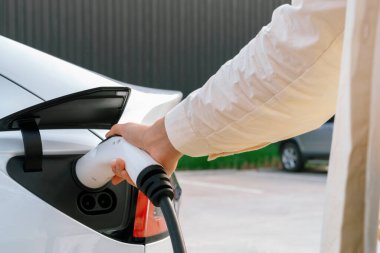 Genç bir kadın şarj aletini şarj istasyonundan elektrikli araba aküsünü şarj etmek için kullanmış. Sürdürülebilir çevre dostu seyahat konsepti için alternatif enerji ve şarj edilebilir EV araba. Yararlı
