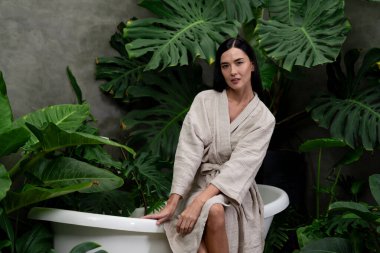 Modern otelde küveti olan tropikal ve egzotik bir spa bahçesi ya da yemyeşil yeşillik arka planıyla çevrili rahat ve sağlıklı yaşam tarzının tadını çıkaran bornozlu bir kadınla tatil köyü. Blithe