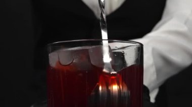Makrografi, kadın bir barmenin becerikli ellerine dikkatle bakın. Siyah arka planda buzlu kırmızı şurubu ustalıkla döküyor. Kadının her yakın çekimi kırmızı bardakta kokteyl hazırlıyor. Geliştirilebilir.
