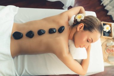 Lüks tatil beldesindeki kaplıca salonunda sıcak taş masajı. Gündüz huzurlu ortam, mutlu kadın müşteri bazalt taşı masajının keyfini çıkarıyor. Sessiz.