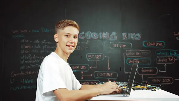 白种人男孩的编码和编程系统 同时看着笔记本电脑屏幕和相机充满自信 坐在黑板前 用计算机分析数据来吸引有魅力的学生 — 图库照片